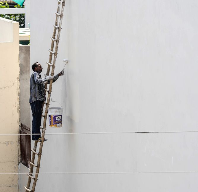 Up a ladder on a rendered wall, one of the parts that decides how long an exterior takes.
